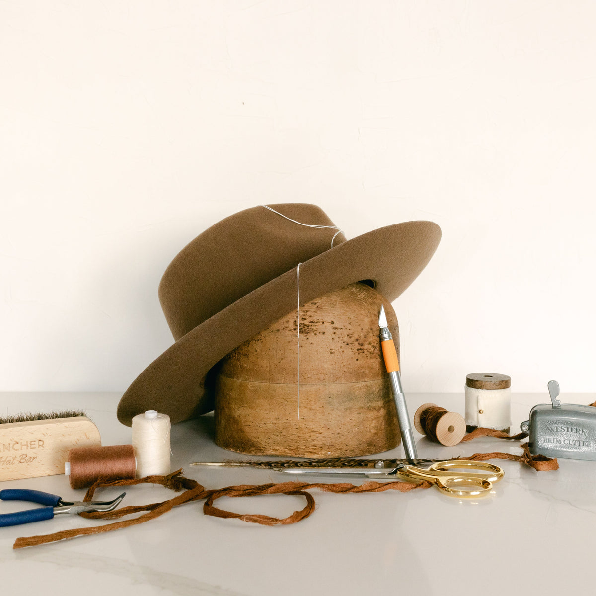 Brown hat on a hat shaper with thread hat making tools and accessories around it