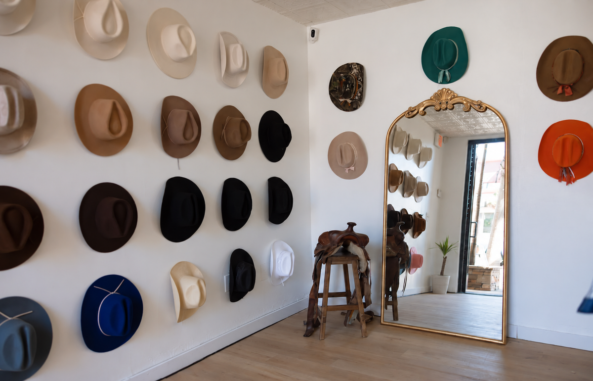 Rancher Hat Bar San Diego interior store image displaying many cowboy-style hats in different colors, arranged in rows. A large ornate gold-framed mirror stands on the floor, reflecting the room and additional hats.