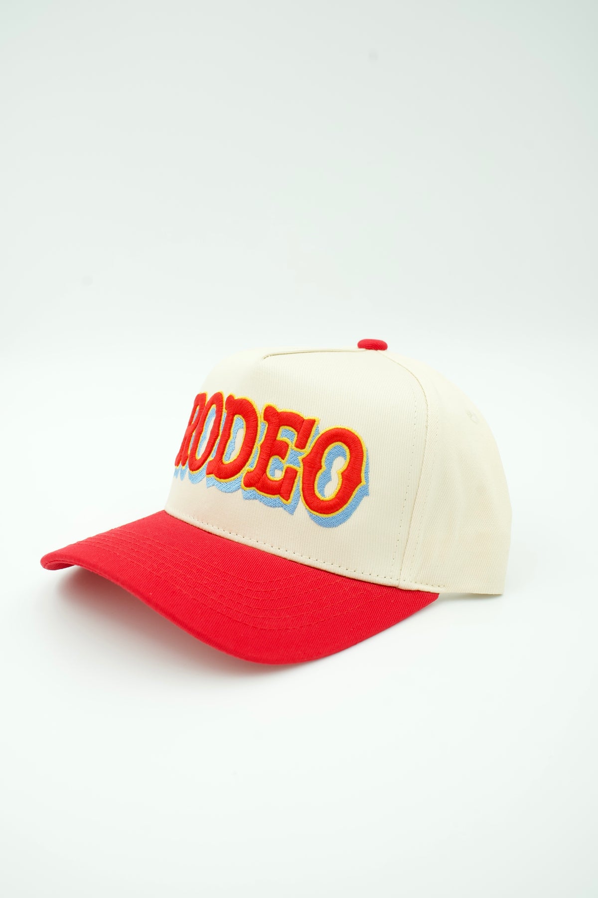 Side image of cream canvas trucker hat with RODEO embroidered in red and light blue with a red bill