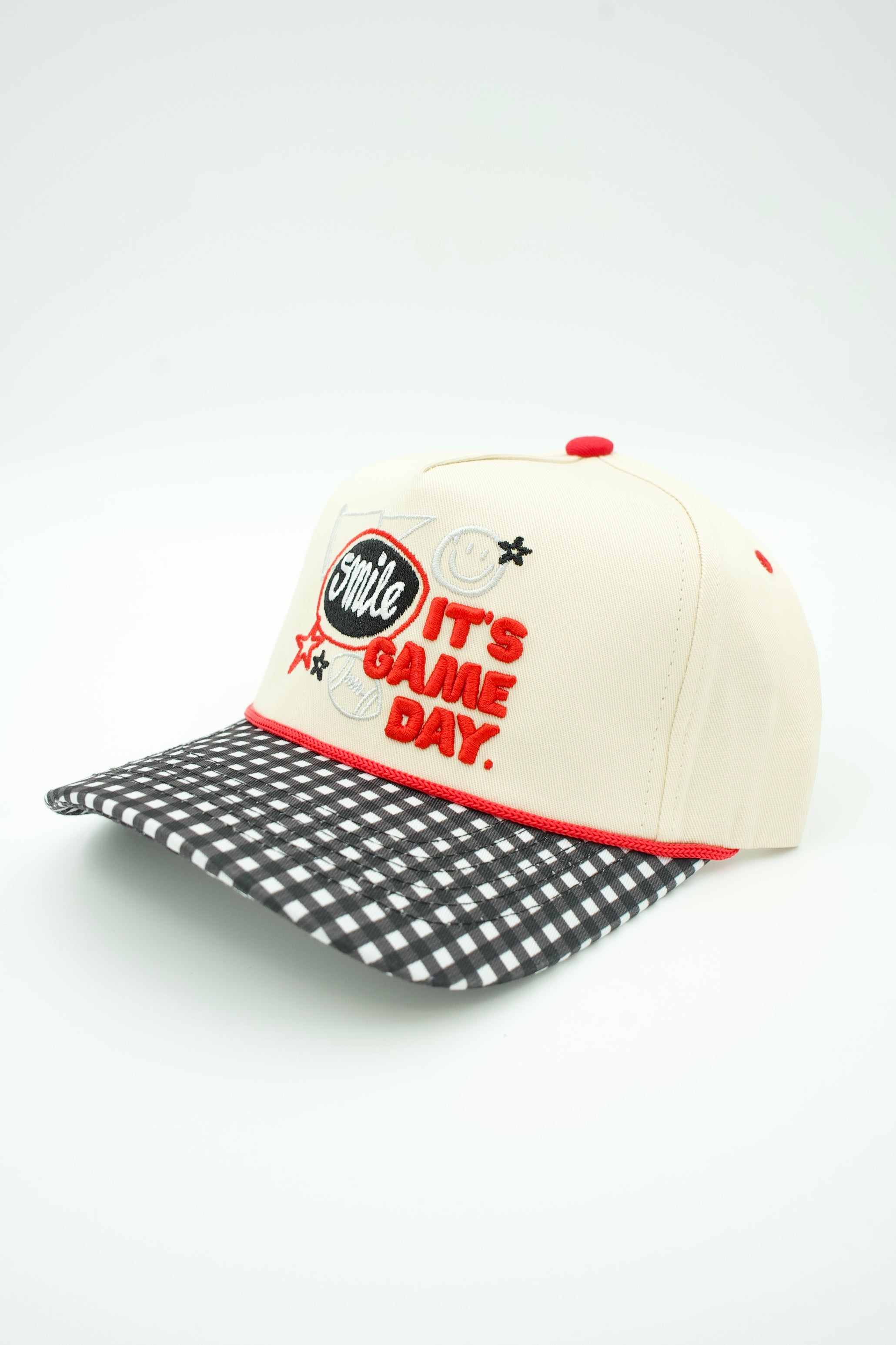 A baseball cap with an off-white crown, red embroidered text reading 'Smile IT'S GAME DAY.', a black-and-white gingham patterned visor, and red trim, shown on a light gray background.