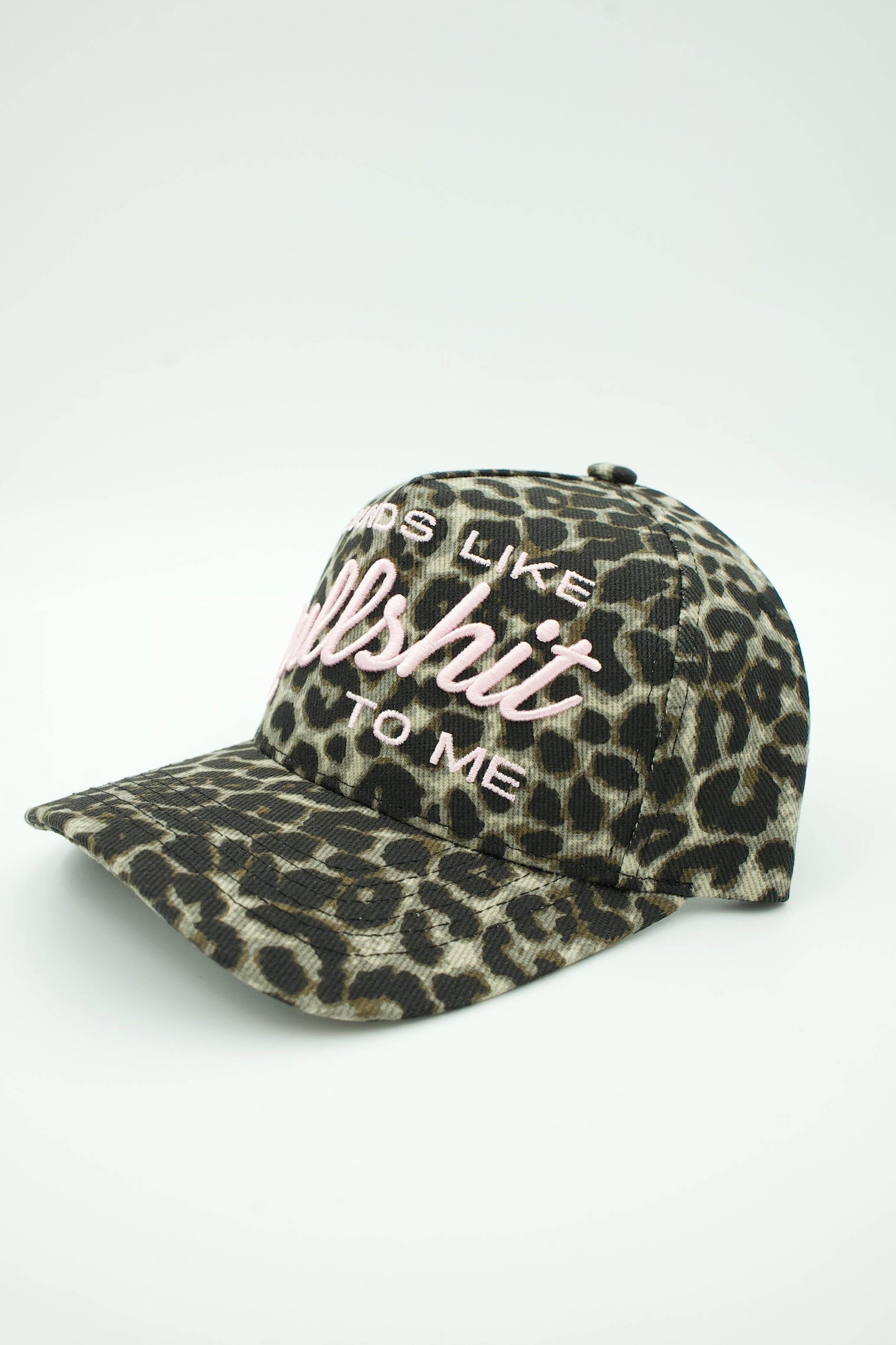 A leopard print baseball cap with pink and white embroidered text reading 'TODS LIKE hellshit TO ME' on a light gray background.
