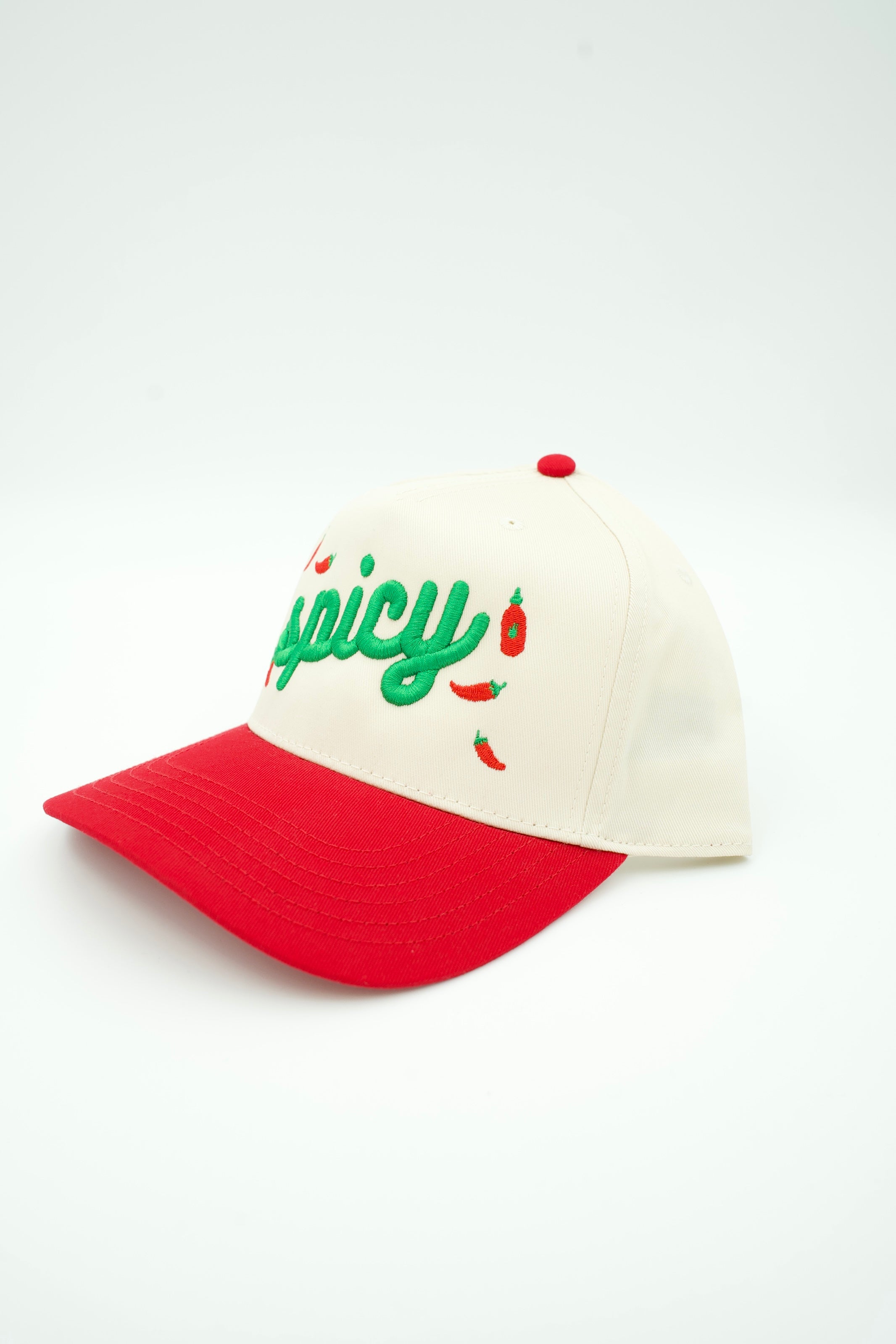 A baseball cap with an off-white crown and a bright red curved brim. The front of the crown features green embroidered text reading 'spicy' with small red chili pepper illustrations.