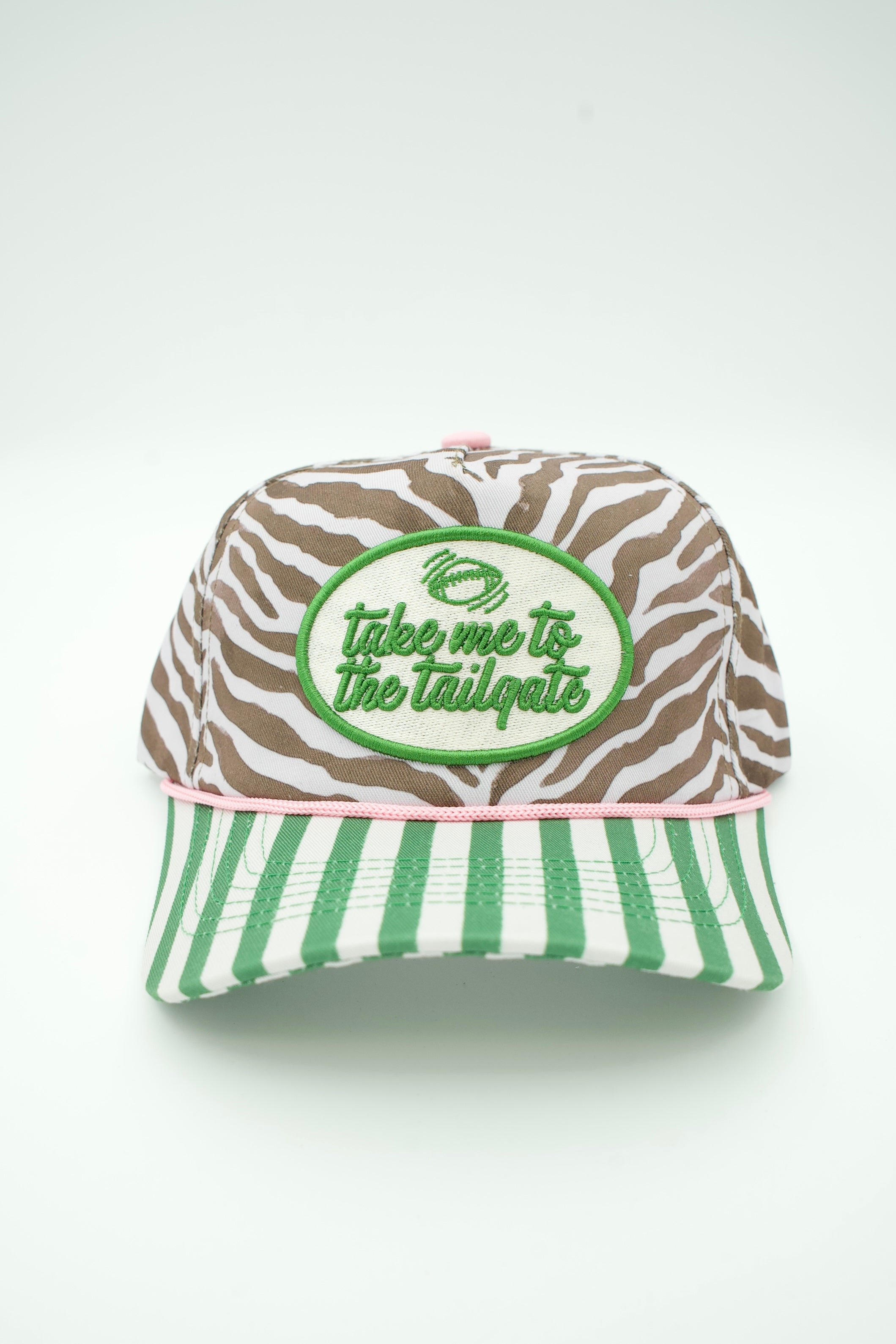 A baseball cap with a brown and white zebra print crown, a green and white striped brim, and a green oval patch on the front that reads 'take me to the tailgate' with a pig logo.