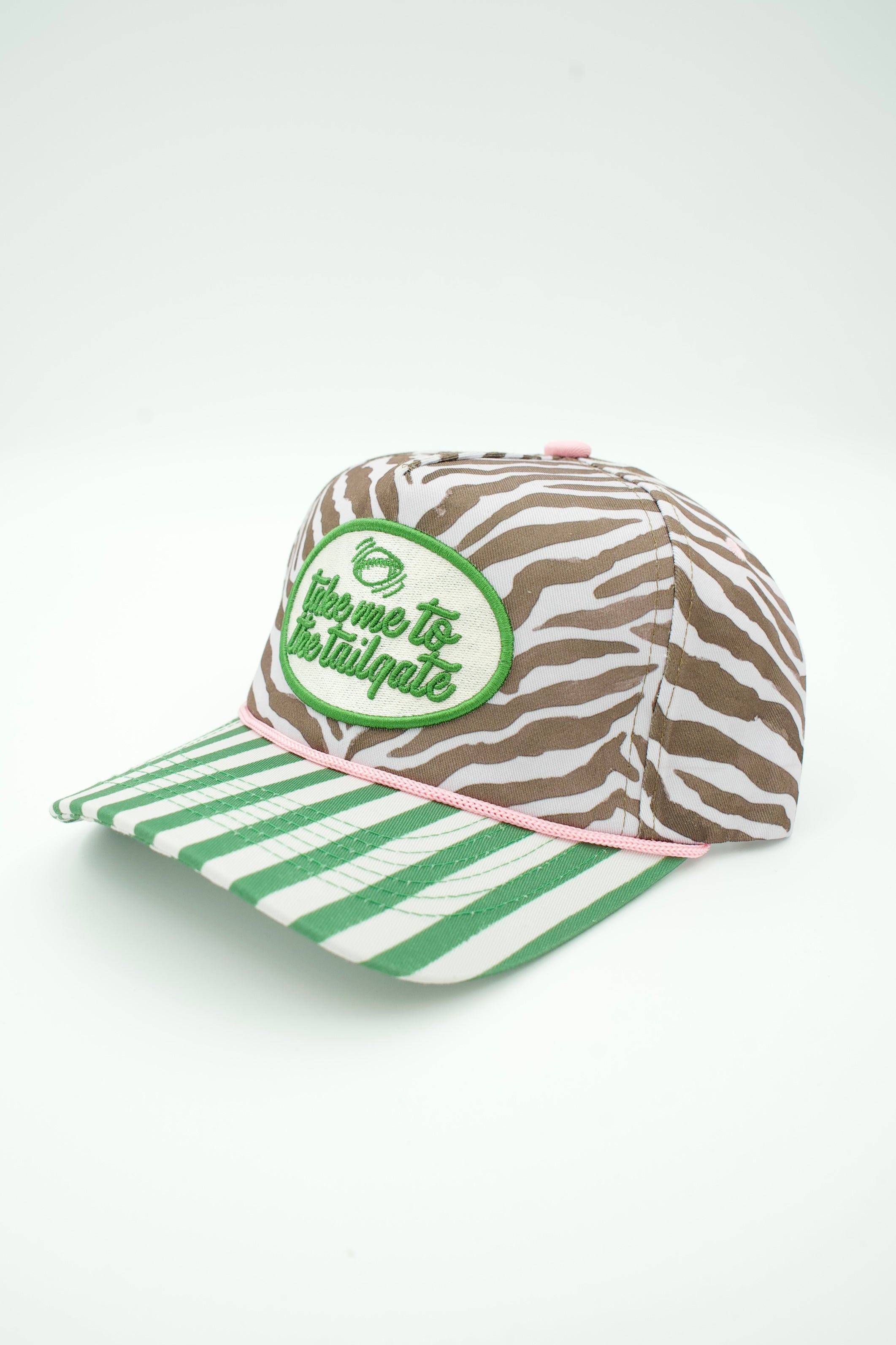 A baseball cap with a brown and white zebra print crown, a green and white striped brim, and a green oval patch on the front that reads 'give me the tailgate'.