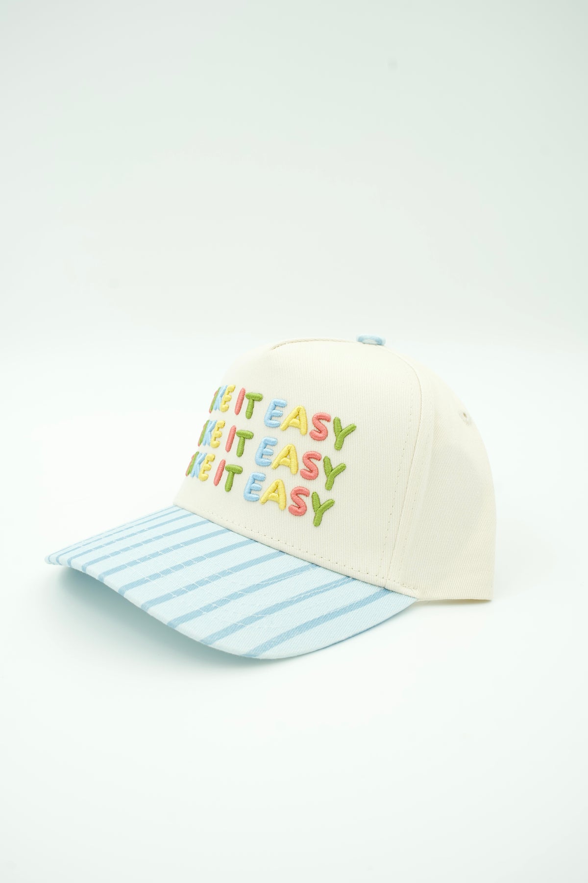 An off-white baseball cap with a light blue and white striped brim. The front of the cap features the phrase 'LET IT EASY' repeated in colorful embroidered letters (red, orange, yellow, green, blue).