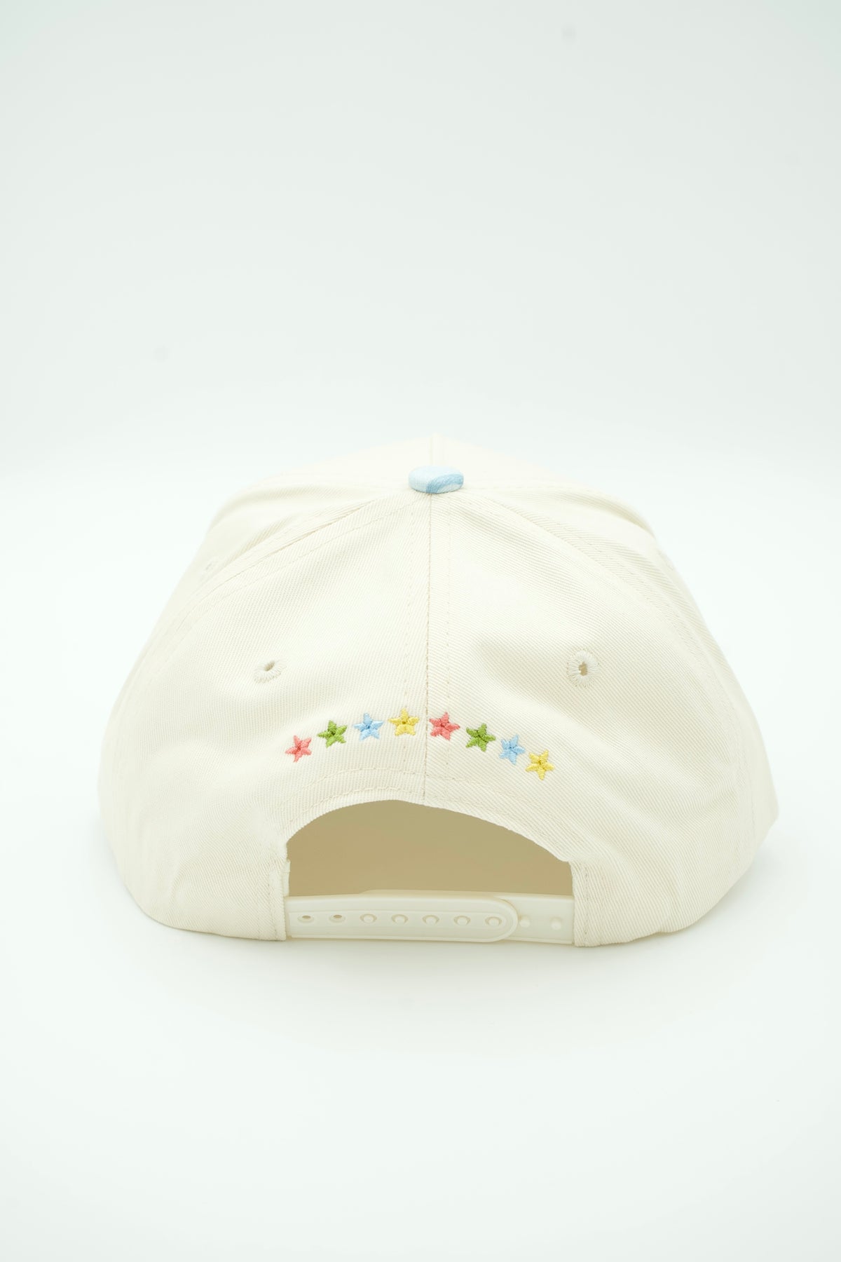 An off-white baseball cap shown from the back, featuring a curved row of small embroidered stars in multiple colors above the back strap.
