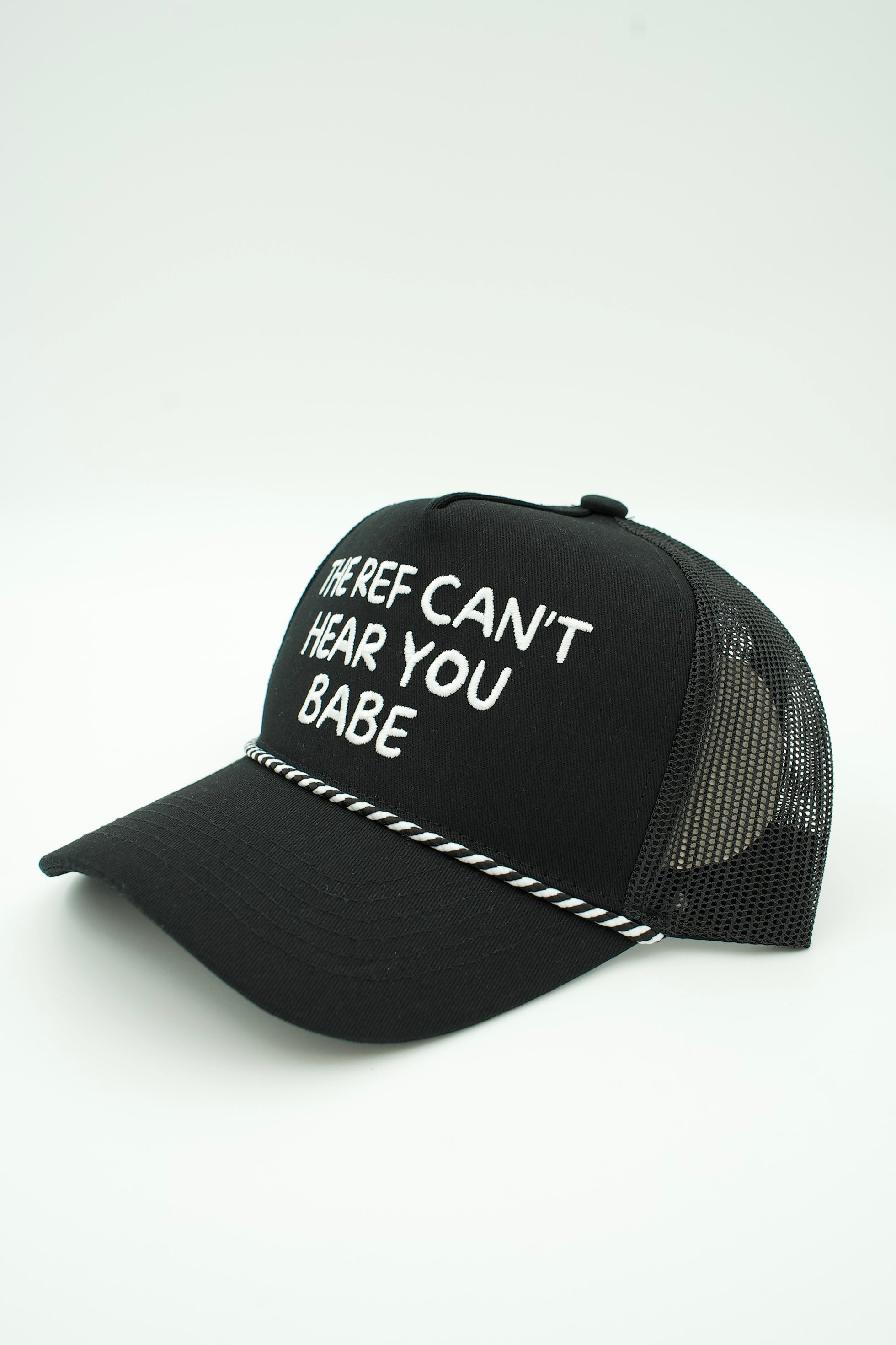 A black trucker-style cap with white embroidered text reading 'HERE'S CAN'T HEAR YOU BABE' and a white dashed line detail on the brim, shown against a plain white background.