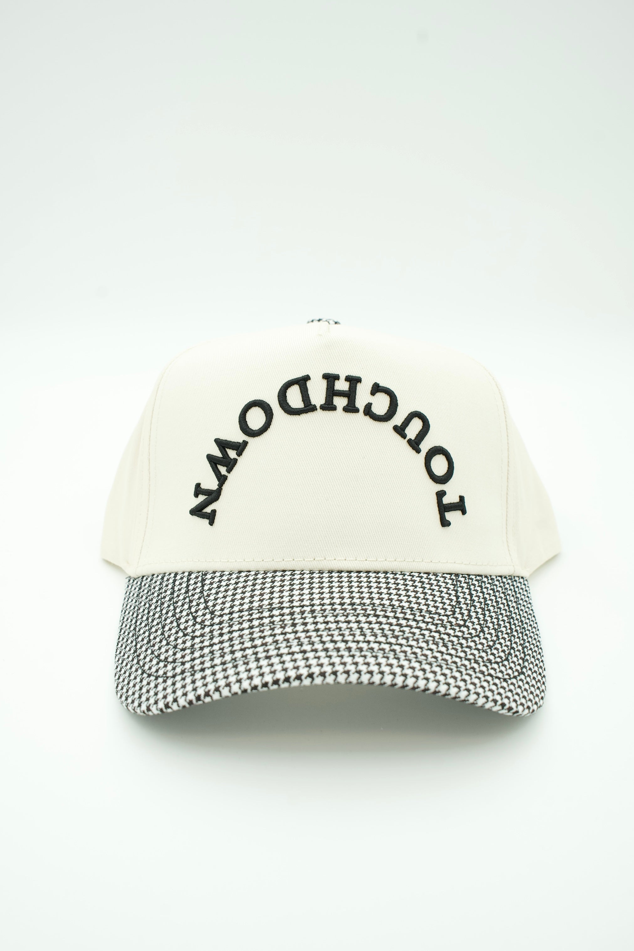 A baseball cap with an off-white crown featuring the word 'TOUCHDOWN' embroidered in black arched text, and a black-and-white houndstooth patterned visor, shown against a plain white background.