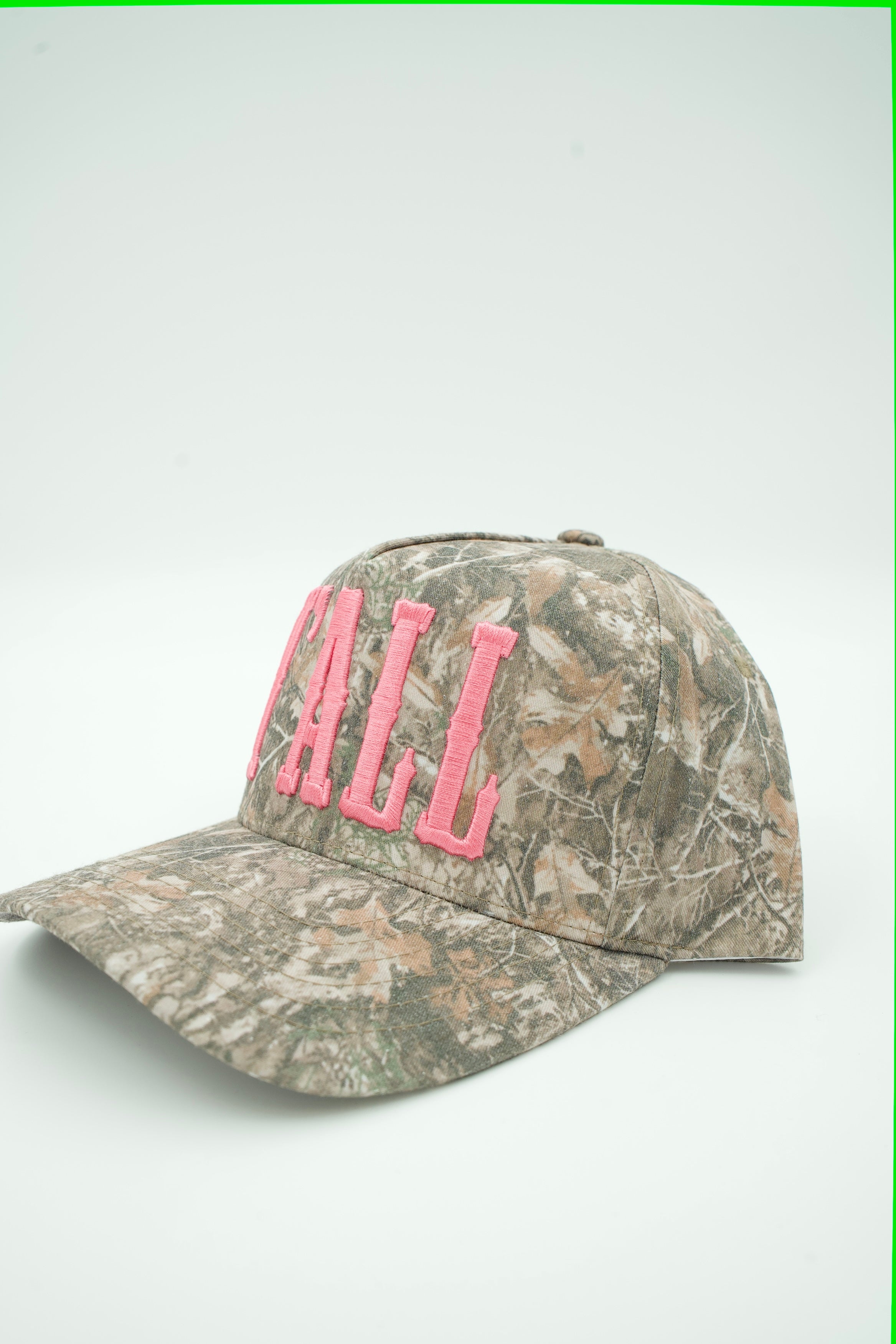 A baseball cap in a brown and beige woodland camouflage pattern, featuring bright pink embroidered letters spelling 'CAMP' on the front.