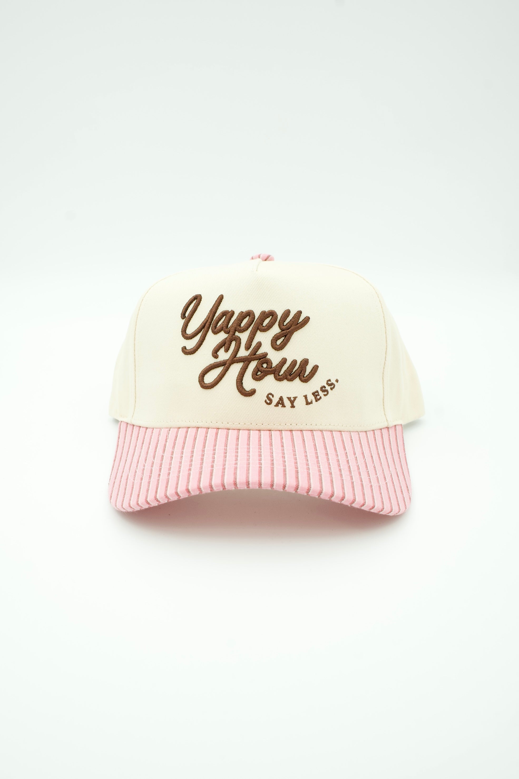 A retro-style baseball cap with an off-white front panel featuring brown embroidered text that reads 'Yappy Hour SAY LESS.' and a pink-and-white vertically striped brim, shown against a plain white background.