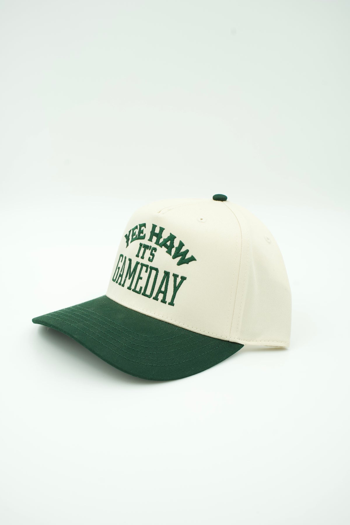 Side image of cream canvas trucker hat with green embroidered "YEE HAW IT'S GAME DAY" and a green bill
