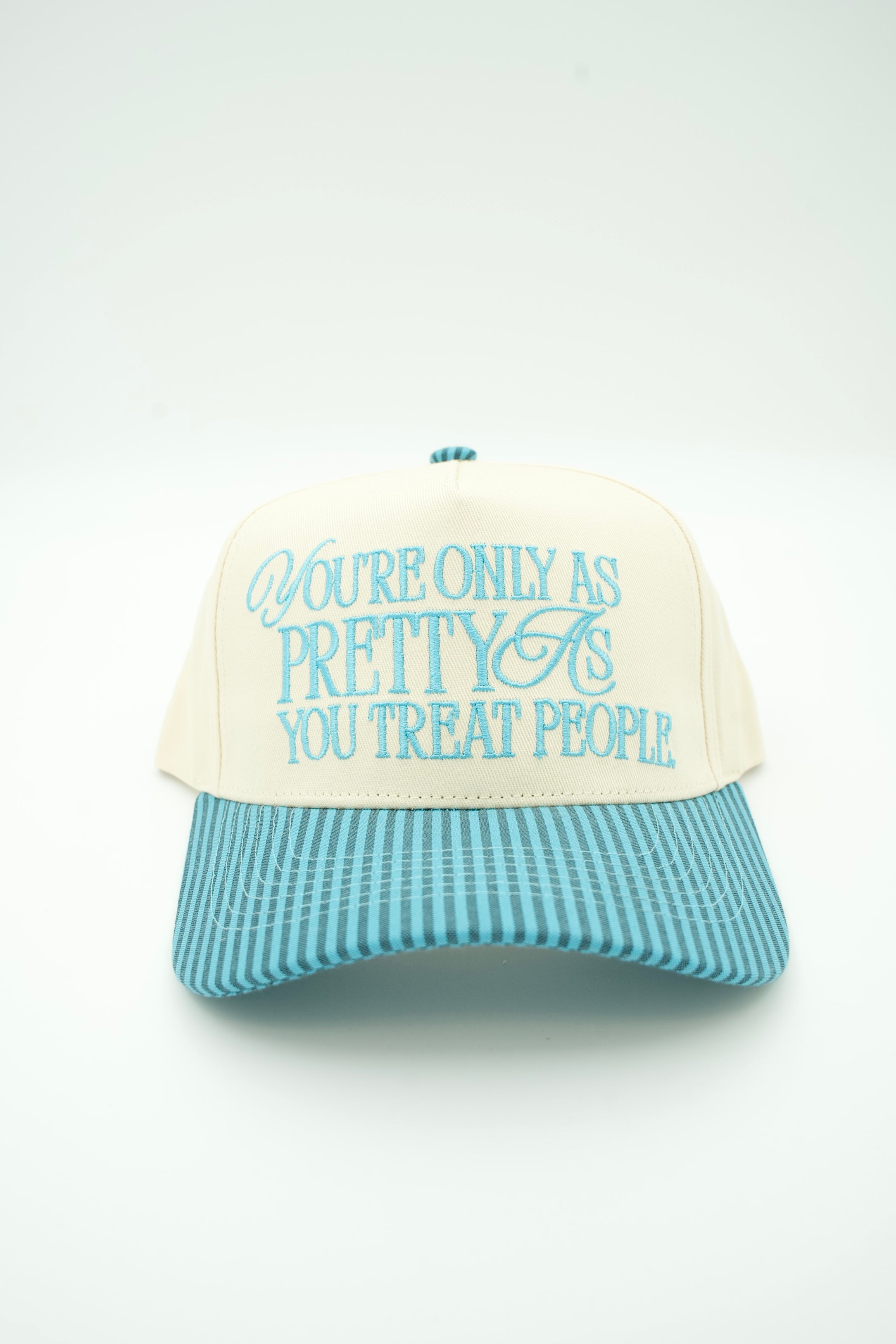 A cream-colored trucker-style cap with a light blue striped brim and light blue embroidered text reading 'You're Only As Pretty As You Treat People' on the front, set against a plain white background.